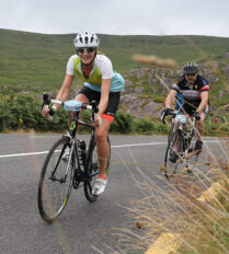 Two cyclists enjoy a scenic ride through lush hills near Killarney on a cloudy day.