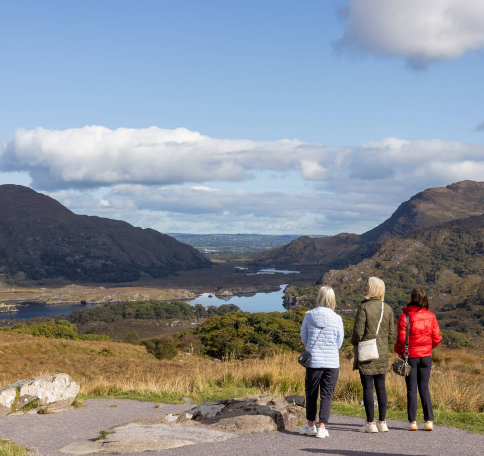 A family enjoys a scenic view of lush hills and lakes near Killarney on a sunny day.
