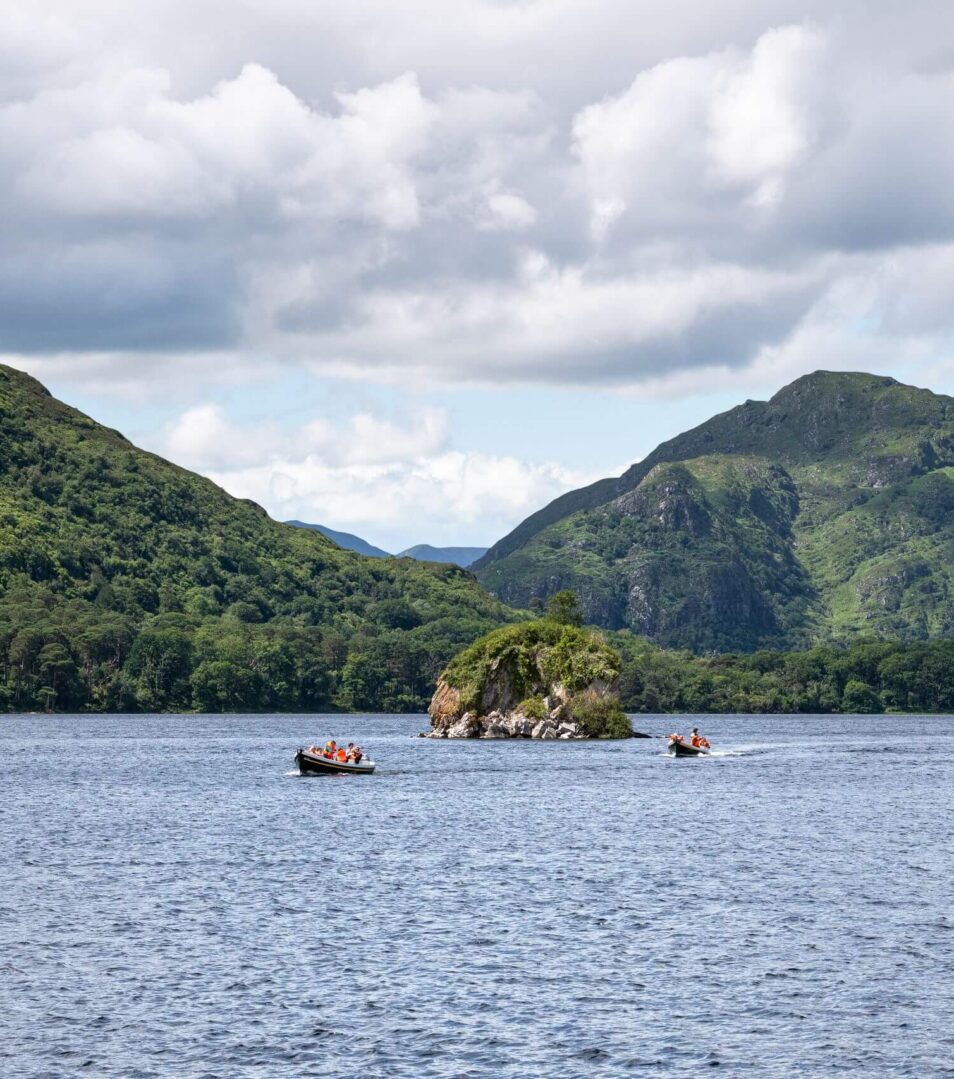 Scenic view of Killarney lake with a group boating, surrounded by lush green hills.