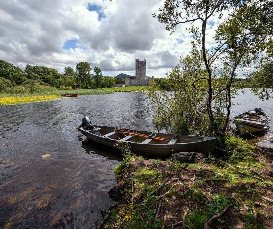 A tranquil lakeside scene with boats, trees, and a castle in Killarney, perfect for family relaxation.