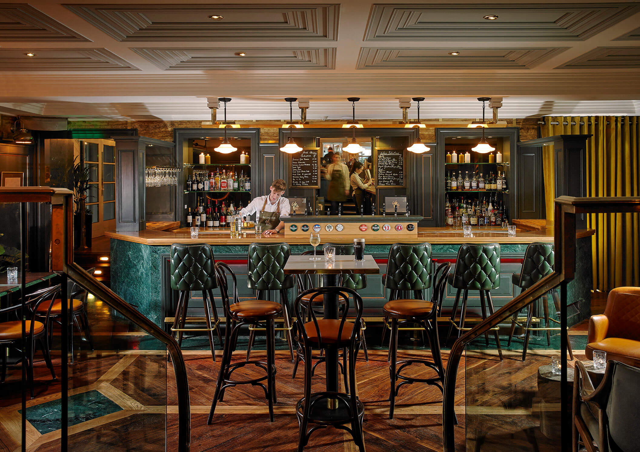 A cosy bar at Park Place Apartments in Killarney with seating and a bartender serving drinks.