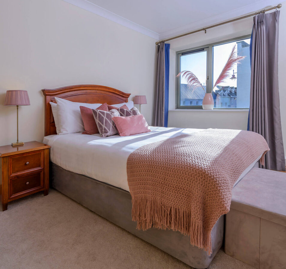 Cozy bedroom in Park Place Apartments, Killarney, with soft pink decor and large window view.