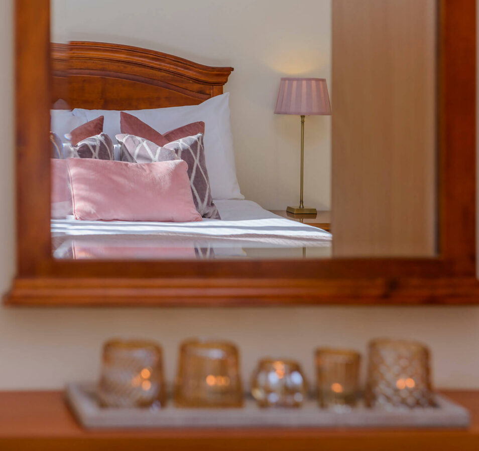 Cosy bedroom with pink cushions reflected in a wooden mirror at Park Place Apartments.