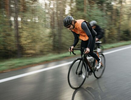 Two cyclists in gear riding through a scenic forest on a peaceful road.