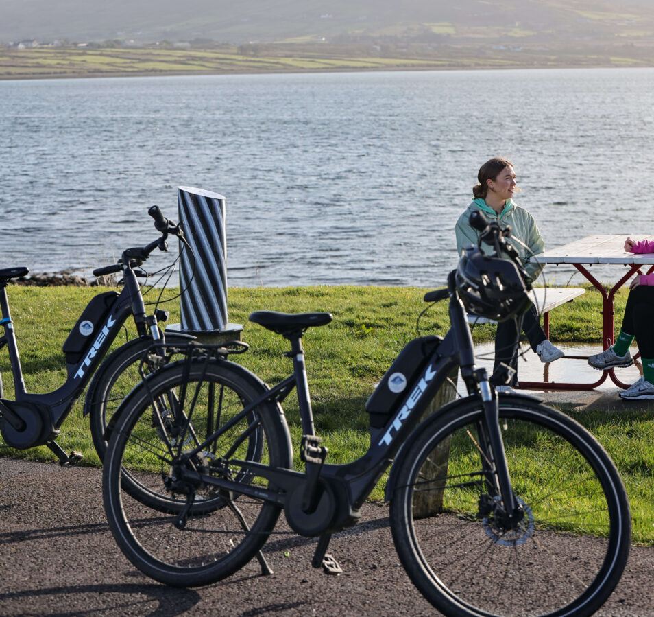 A couple enjoys a picnic by the lake with bicycles parked nearby, offering a serene view.