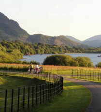 A family cycles along a scenic path beside a lake and hills near Killarney.