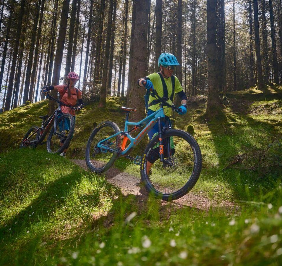 A couple cycling through a sunlit forest near Killarney town, enjoying the lush greenery.