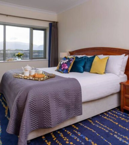 Cozy bedroom with breakfast tray, colourful pillows, and a scenic mountain view at a window.