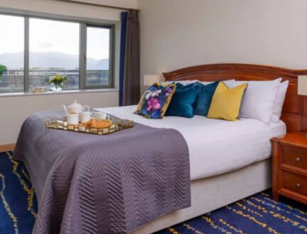 Cozy bedroom with breakfast tray, colourful pillows, and a scenic mountain view at a window.