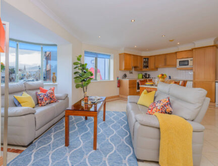 Modern living area in Park Place Apartments with cosy sofas, a bright window view, and a full kitchen setup.