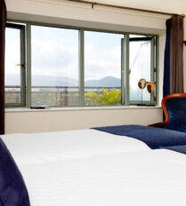Cosy bedroom with twin beds, a large window offering scenic views of Killarney's lush landscape.