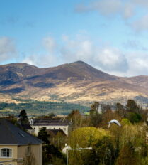 View of Killarney with mountains and church against a bright blue sky.