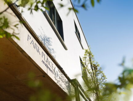 Modern Park Place Apartments facade with lush greenery and sunny blue sky in Killarney Town.