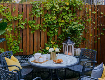 Cosy patio at Park Place Apartments with garden, table set for breakfast and colourful sky.