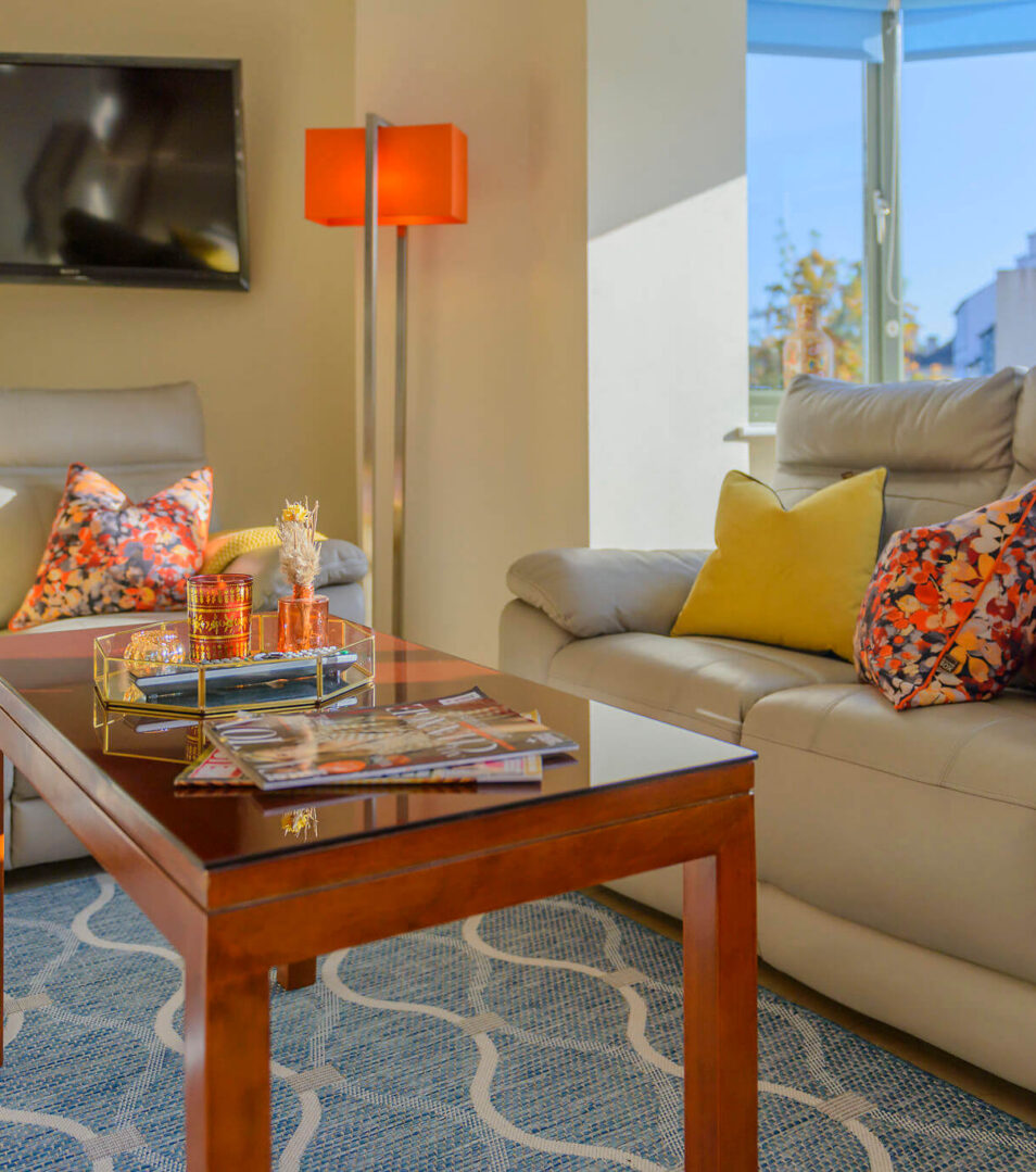 Modern, cosy living room with soft sofas, colourful cushions, and warm natural light.