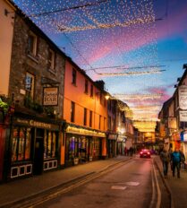 A lively street in Killarney with festive lights, shops, and people enjoying an evening stroll.
