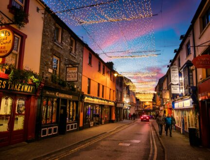 A lively street in Killarney with festive lights, shops, and people enjoying an evening stroll.