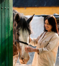 A smiling woman gently strokes a horse near a stable at Park Place Apartments, Killarney.