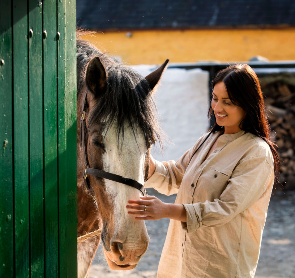 A smiling woman gently strokes a horse near a stable at Park Place Apartments, Killarney.