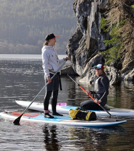 A couple paddleboards on a serene lake in Killarney, surrounded by lush greenery and rocky cliffs.