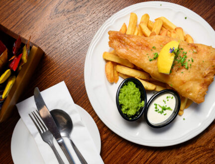 Delicious fish and chips with sauces on a wooden table at Park Place Apartments restaurant.