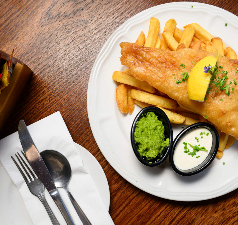Delicious fish and chips with sauces on a wooden table at Park Place Apartments restaurant.