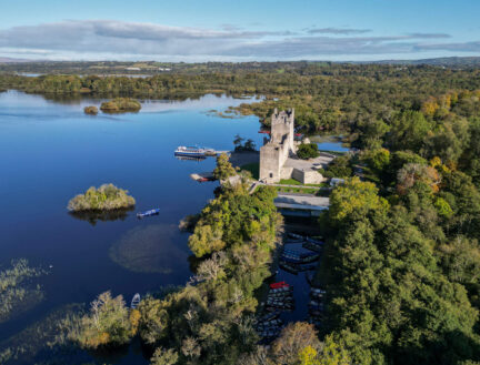 Scenic aerial view of a serene lake with a historic stone castle surrounded by lush greenery, a perfect setting for family exploration.