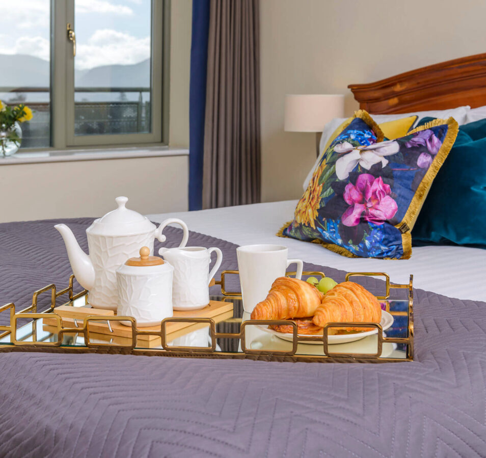 Cosy bedroom with breakfast tray featuring tea and croissants at Park Place Apartments, Killarney.