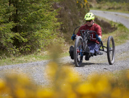 Person cycling on a gravel path through a lush green forest.