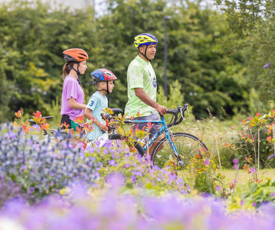 Family enjoying a bike ride through colourful gardens at Park Place Apartments, Killarney.